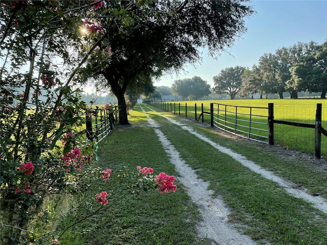 view of property's community with driveway, a rural view, fence, and a lawn