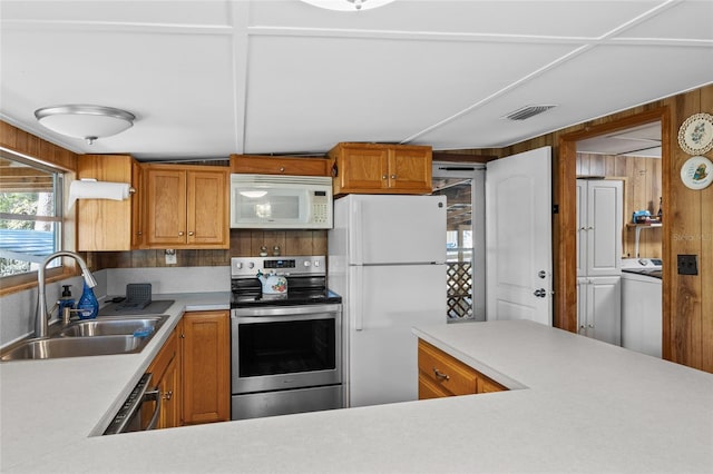 kitchen featuring a sink, white appliances, wooden walls, light countertops, and washer / dryer