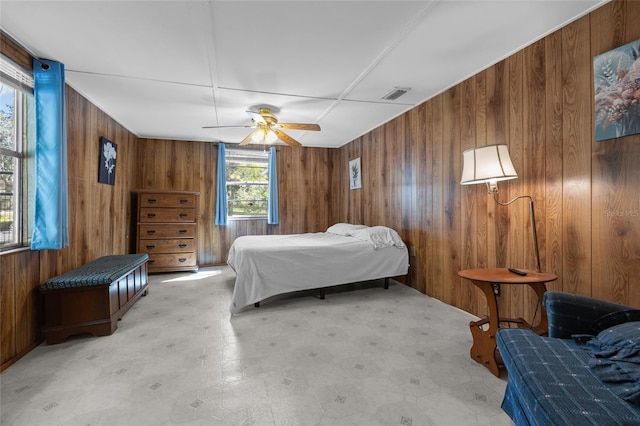 bedroom featuring wooden walls, a ceiling fan, and visible vents