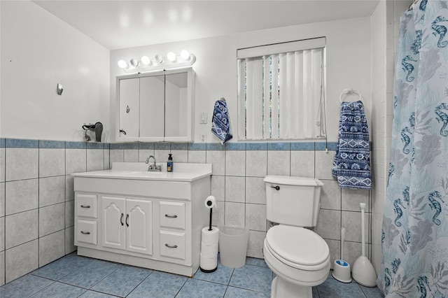 bathroom featuring tile patterned flooring, toilet, vanity, wainscoting, and tile walls