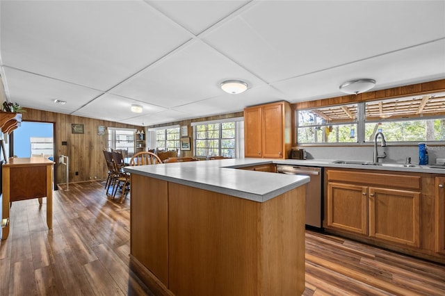 kitchen featuring a sink, stainless steel dishwasher, wooden walls, light countertops, and dark wood-style flooring