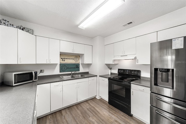 kitchen with under cabinet range hood, stainless steel appliances, a sink, white cabinets, and dark countertops