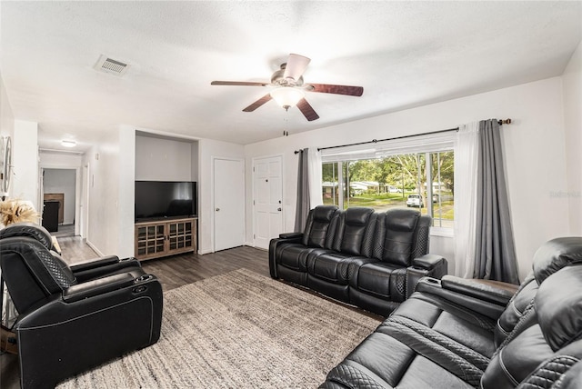 living room with ceiling fan, a textured ceiling, visible vents, and dark wood-style flooring