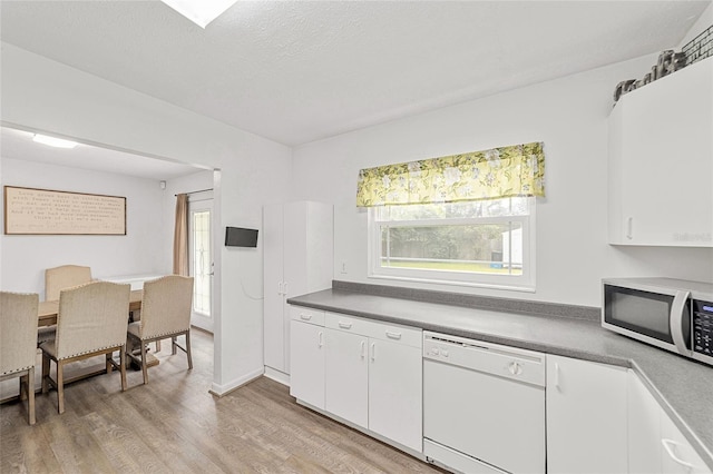 kitchen featuring stainless steel microwave, light wood-style flooring, white cabinets, white dishwasher, and a textured ceiling