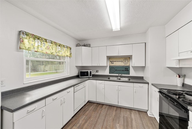 kitchen featuring stainless steel microwave, dark countertops, a sink, and white cabinets