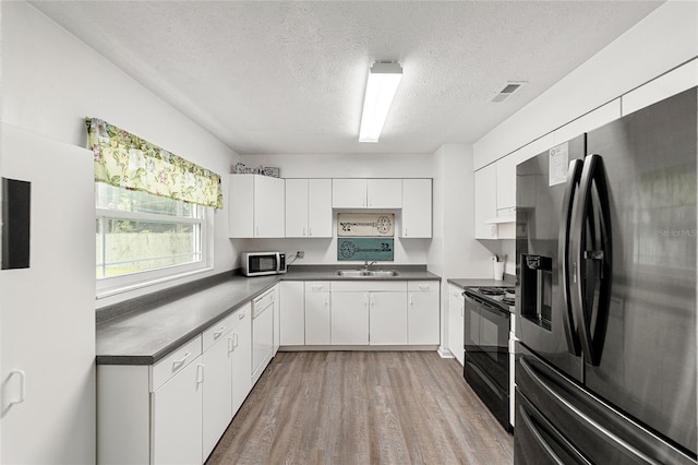 kitchen featuring stainless steel appliances, dark countertops, visible vents, white cabinets, and light wood-type flooring