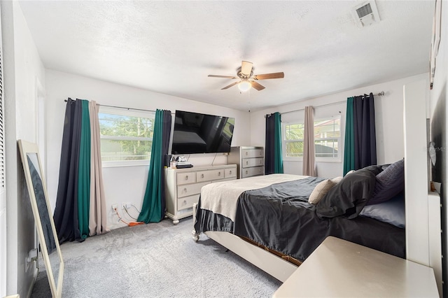 bedroom featuring light colored carpet, visible vents, a textured ceiling, and multiple windows