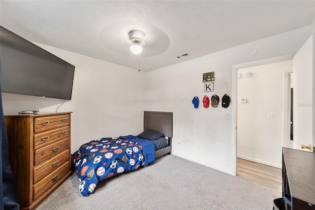 bedroom featuring a textured ceiling, light carpet, visible vents, a ceiling fan, and baseboards