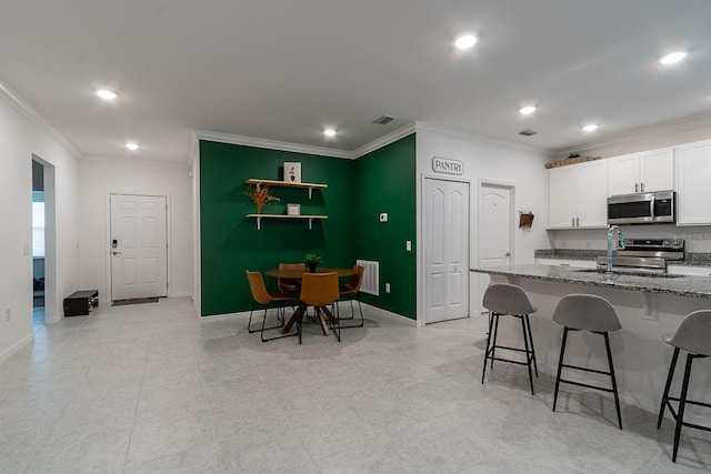 kitchen with crown molding, stone countertops, a kitchen bar, white cabinetry, and stainless steel appliances