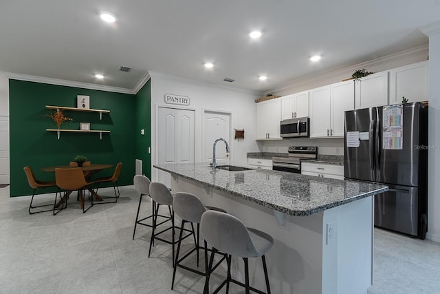 kitchen with sink, dark stone countertops, an island with sink, white cabinetry, and stainless steel appliances