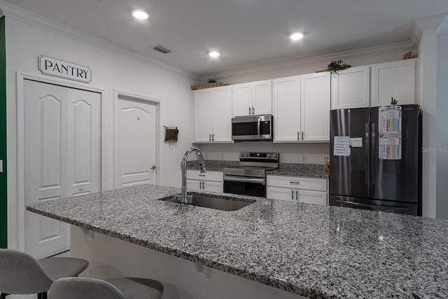 kitchen featuring white cabinetry, sink, dark stone counters, a breakfast bar area, and appliances with stainless steel finishes