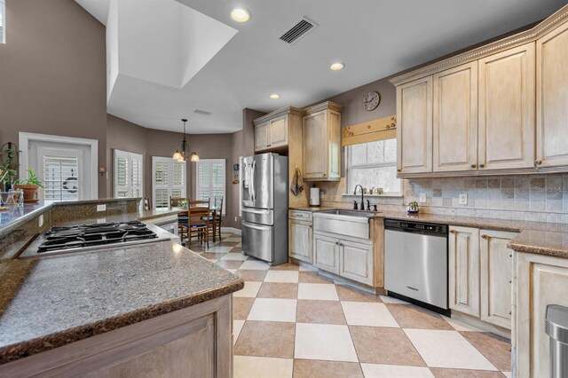 kitchen with backsplash, sink, appliances with stainless steel finishes, a chandelier, and light tile patterned floors