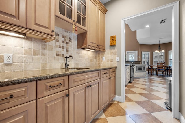 kitchen with stainless steel stove, tasteful backsplash, light tile patterned floors, sink, and decorative light fixtures