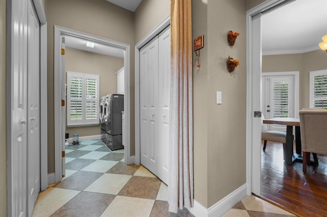 hallway featuring independent washer and dryer, plenty of natural light, light tile patterned flooring, and ornamental molding