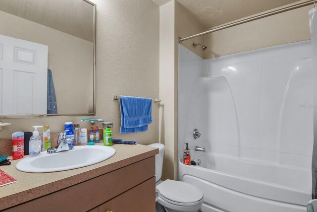 full bath featuring toilet,  shower combination, vanity, and a textured wall