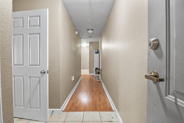 hallway featuring a textured wall, baseboards, a textured ceiling, and tile patterned flooring