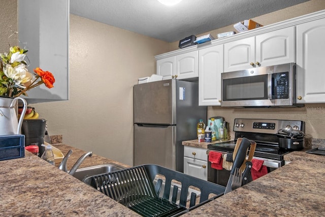 kitchen with stainless steel appliances, a textured wall, white cabinetry, a textured ceiling, and dark countertops
