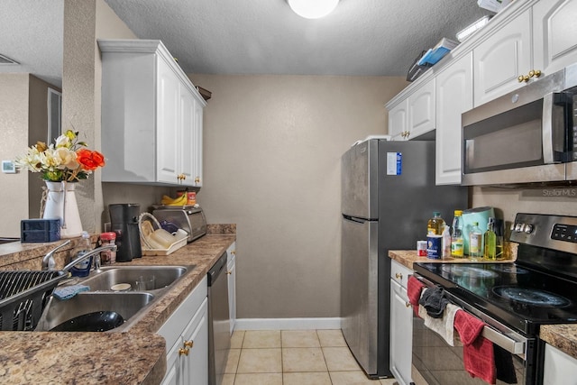 kitchen featuring appliances with stainless steel finishes, a sink, white cabinetry, a textured ceiling, and baseboards