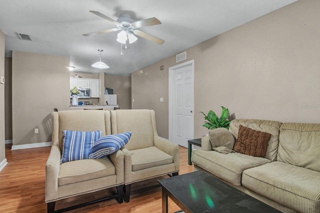 living area featuring a ceiling fan, light wood-style flooring, and baseboards