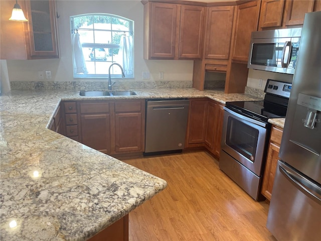 kitchen featuring appliances with stainless steel finishes, sink, hanging light fixtures, light hardwood / wood-style floors, and light stone countertops