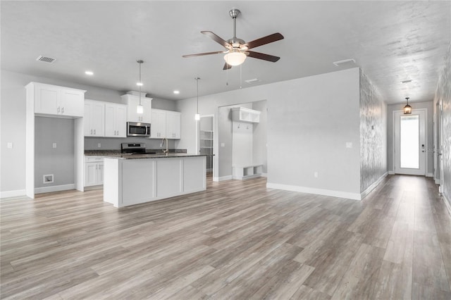 kitchen featuring white cabinetry, light hardwood / wood-style flooring, a center island with sink, dark stone countertops, and stainless steel appliances