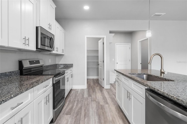 kitchen featuring sink, appliances with stainless steel finishes, white cabinetry, hanging light fixtures, and dark stone counters