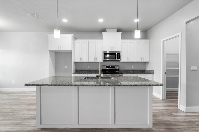 kitchen featuring dark stone countertops, a kitchen island with sink, white cabinets, and appliances with stainless steel finishes