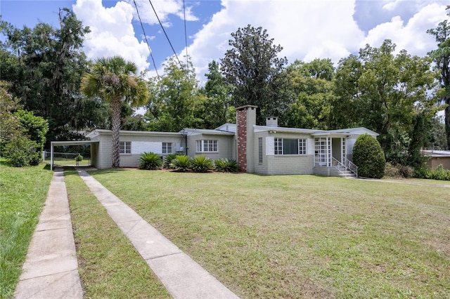 view of front of property featuring brick siding, a chimney, a carport, and a front yard