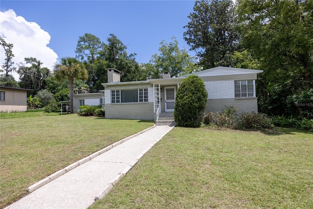 single story home featuring brick siding, a front lawn, and a chimney