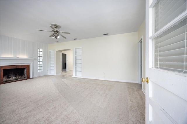 unfurnished living room featuring visible vents, arched walkways, a tiled fireplace, carpet flooring, and built in shelves