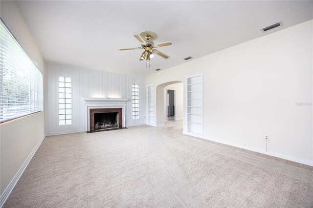 unfurnished living room with ceiling fan, a tiled fireplace, light carpet, and built in features