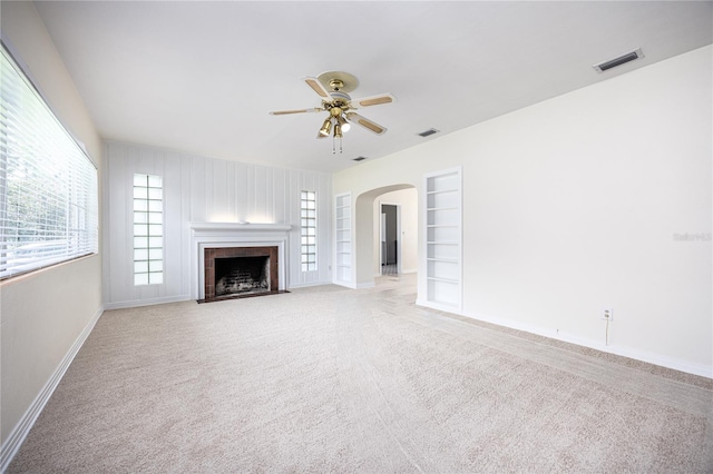 unfurnished living room featuring built in features, visible vents, a ceiling fan, a fireplace with flush hearth, and carpet flooring