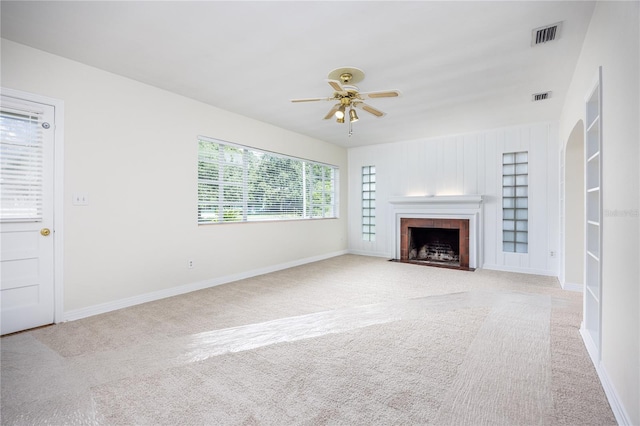 unfurnished living room with carpet flooring, a fireplace with flush hearth, visible vents, and a ceiling fan