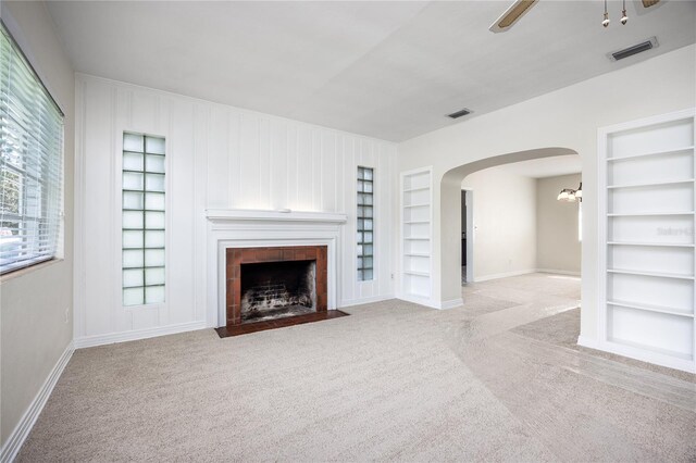 unfurnished living room with light carpet, built in shelves, and a tiled fireplace