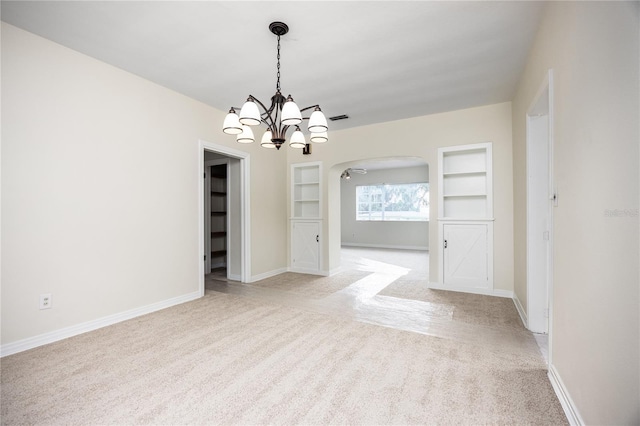 empty room with baseboards, built in features, arched walkways, and light colored carpet