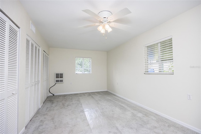 unfurnished bedroom featuring baseboards, visible vents, a ceiling fan, carpet floors, and multiple closets