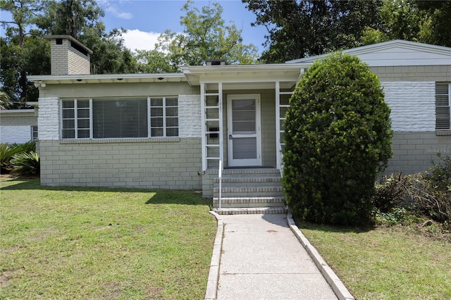 view of front of home featuring entry steps, a chimney, and a front lawn