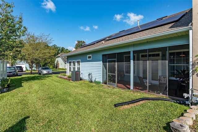 10545 NW 30th Ln, Gainesville, FL 32606 - back of house with central air condition unit, a lawn, a shingled roof, roof mounted solar panels, and a sunroom