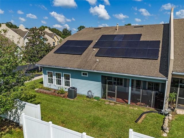 back of property featuring a sunroom, solar panels, cooling unit, and a yard