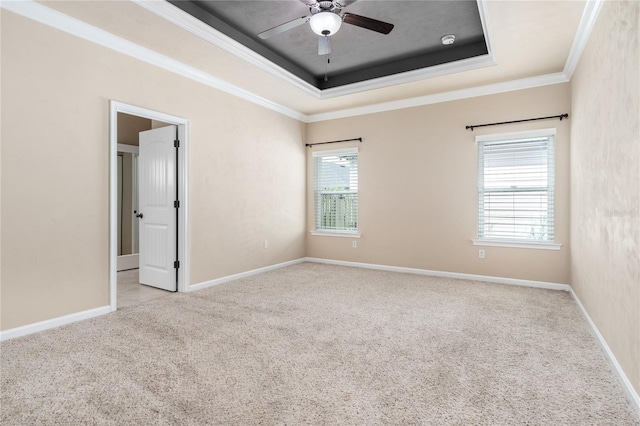 carpeted empty room with a raised ceiling, crown molding, a healthy amount of sunlight, and ceiling fan