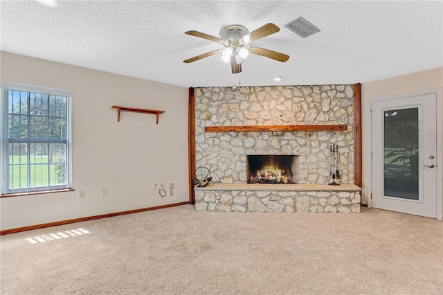 unfurnished living room with ceiling fan, a stone fireplace, and light colored carpet