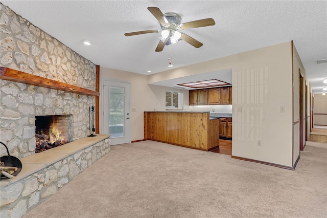 unfurnished living room with a fireplace, ceiling fan, a textured ceiling, and light colored carpet