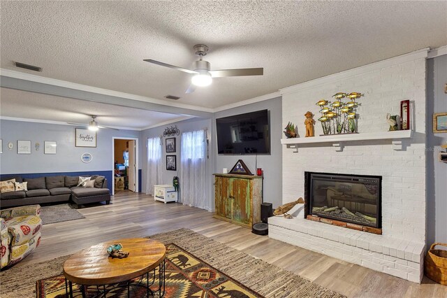 living room with ceiling fan, a brick fireplace, wood-type flooring, a textured ceiling, and crown molding