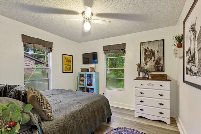 bedroom with multiple windows, light wood-type flooring, a textured ceiling, and ceiling fan