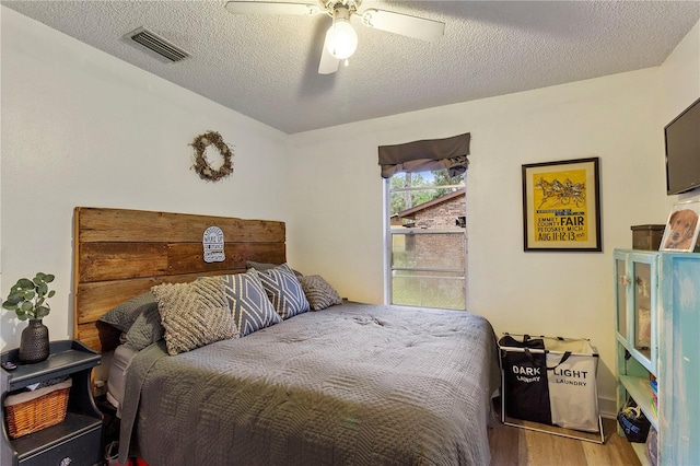 bedroom with a ceiling fan, a textured ceiling, visible vents, and wood finished floors