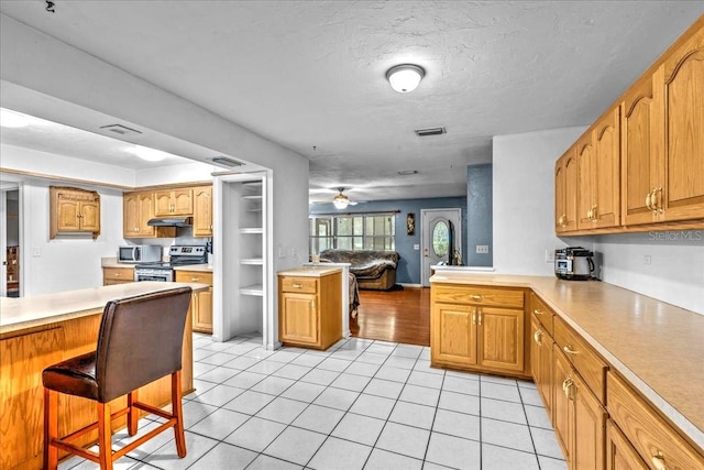 kitchen featuring stainless steel appliances, light hardwood / wood-style floors, kitchen peninsula, ceiling fan, and a breakfast bar area