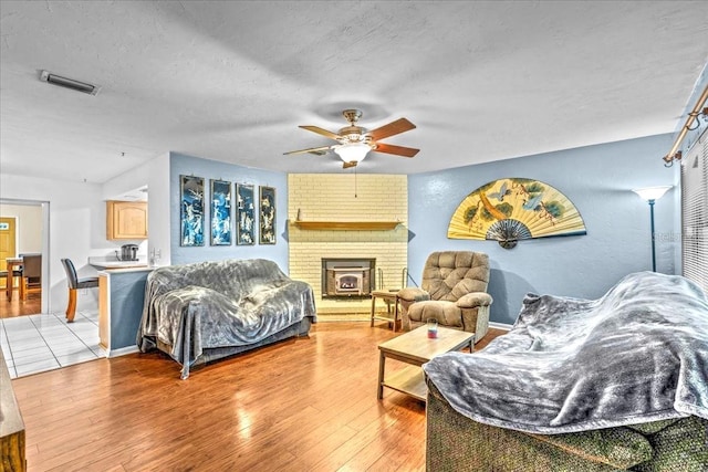 living room featuring hardwood / wood-style floors, brick wall, a textured ceiling, ceiling fan, and a brick fireplace