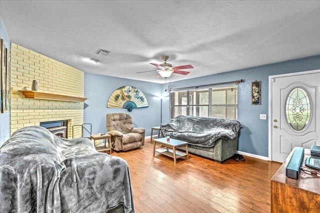 living room with a fireplace, hardwood / wood-style flooring, a textured ceiling, ceiling fan, and brick wall