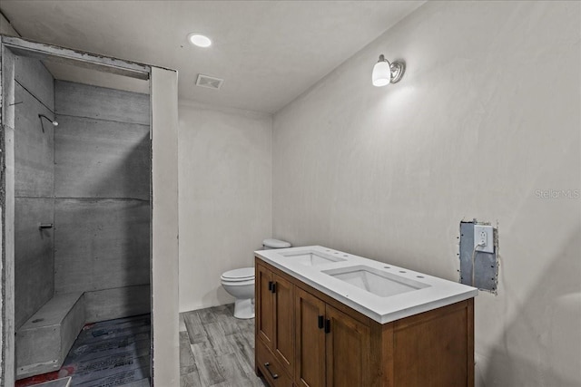 bathroom with hardwood / wood-style flooring, vanity, walk in shower, and toilet