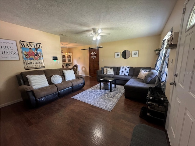 living room featuring ceiling fan, dark wood-type flooring, a textured ceiling, and a barn door